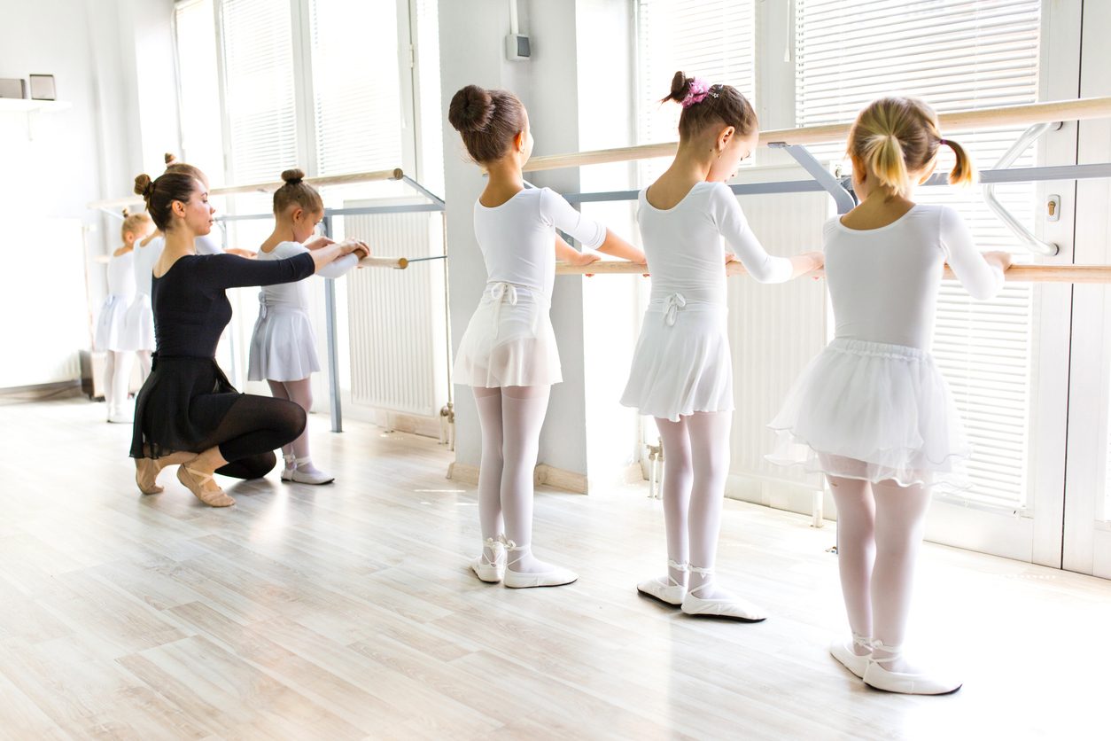 Little girls  are having ballet class with personal ballet teacher in a dance studio. She is helping them improve their postures.